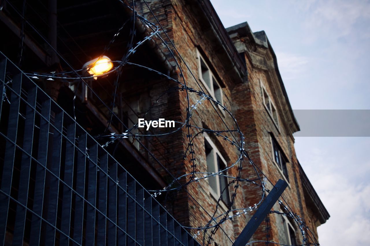 Low angle view of fence by building against sky 