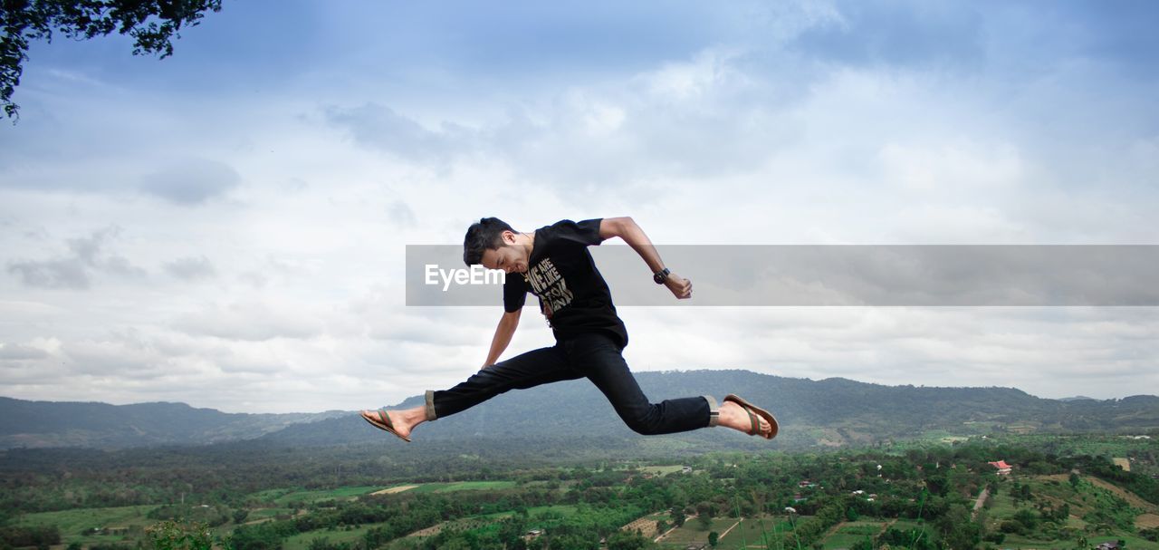 Side view of young man jumping against mountain