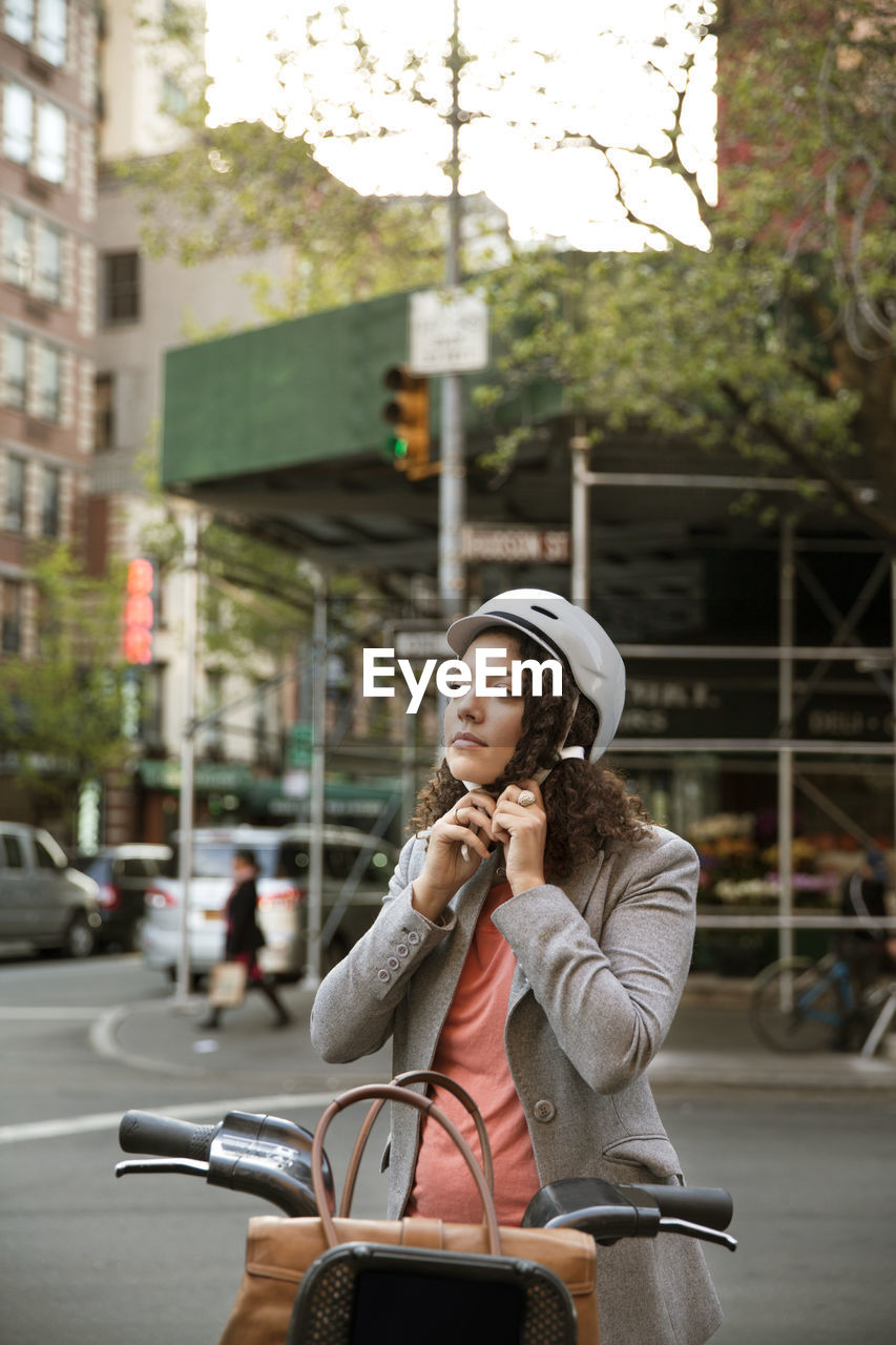 Businesswoman wearing helmet while standing by bicycle on street