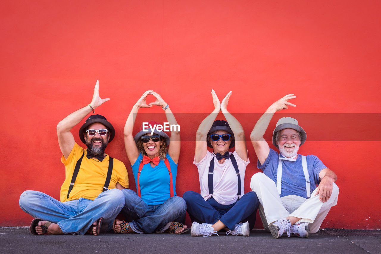 Portrait of smiling friends with arms raised sitting against red wall