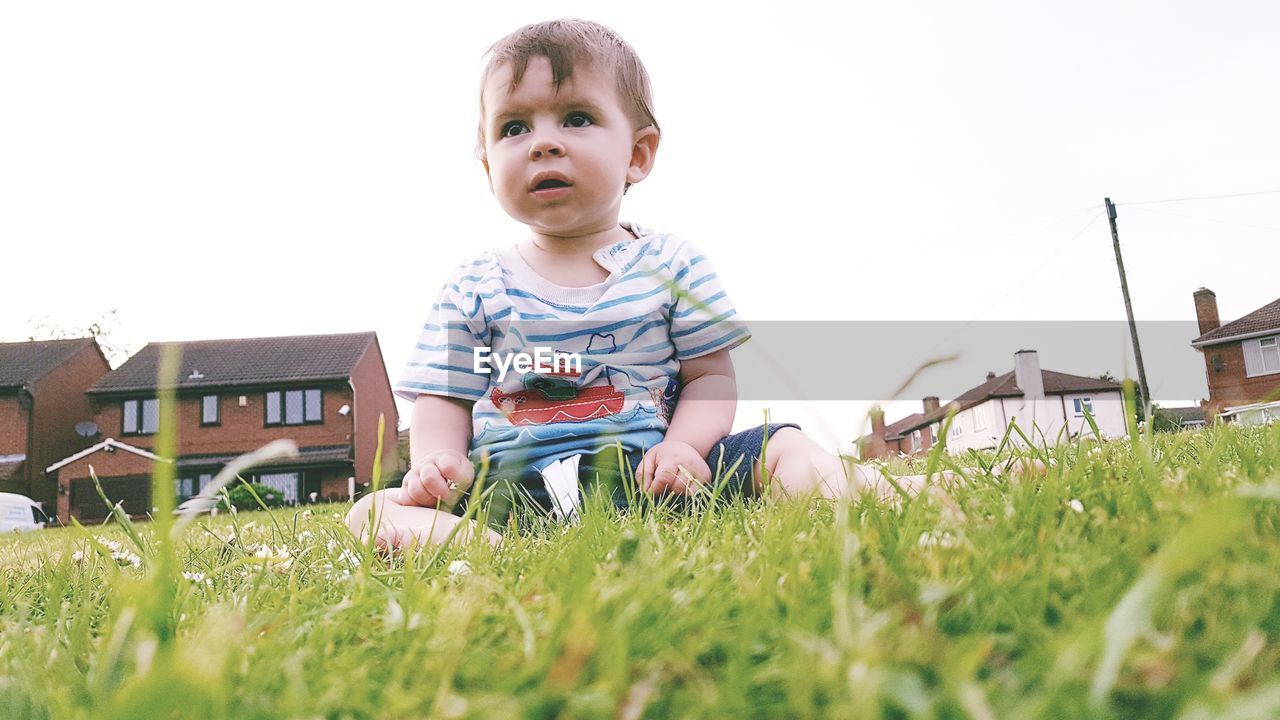 Cute boy sitting on grass against sky