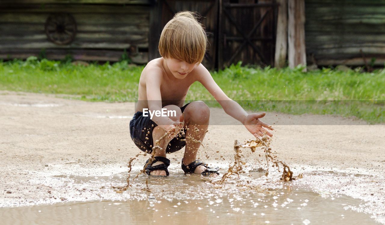 Full length of shirtless boy playing with muddy water