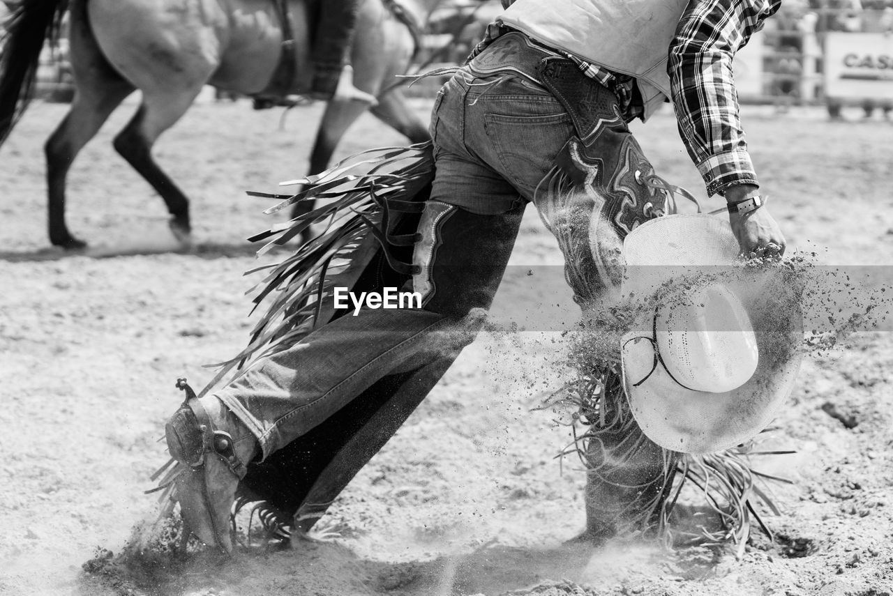 Low section of cowboy with hat walking on sand