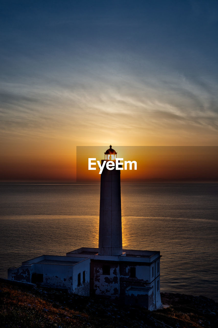 Lighthouse by sea against sky at dawn