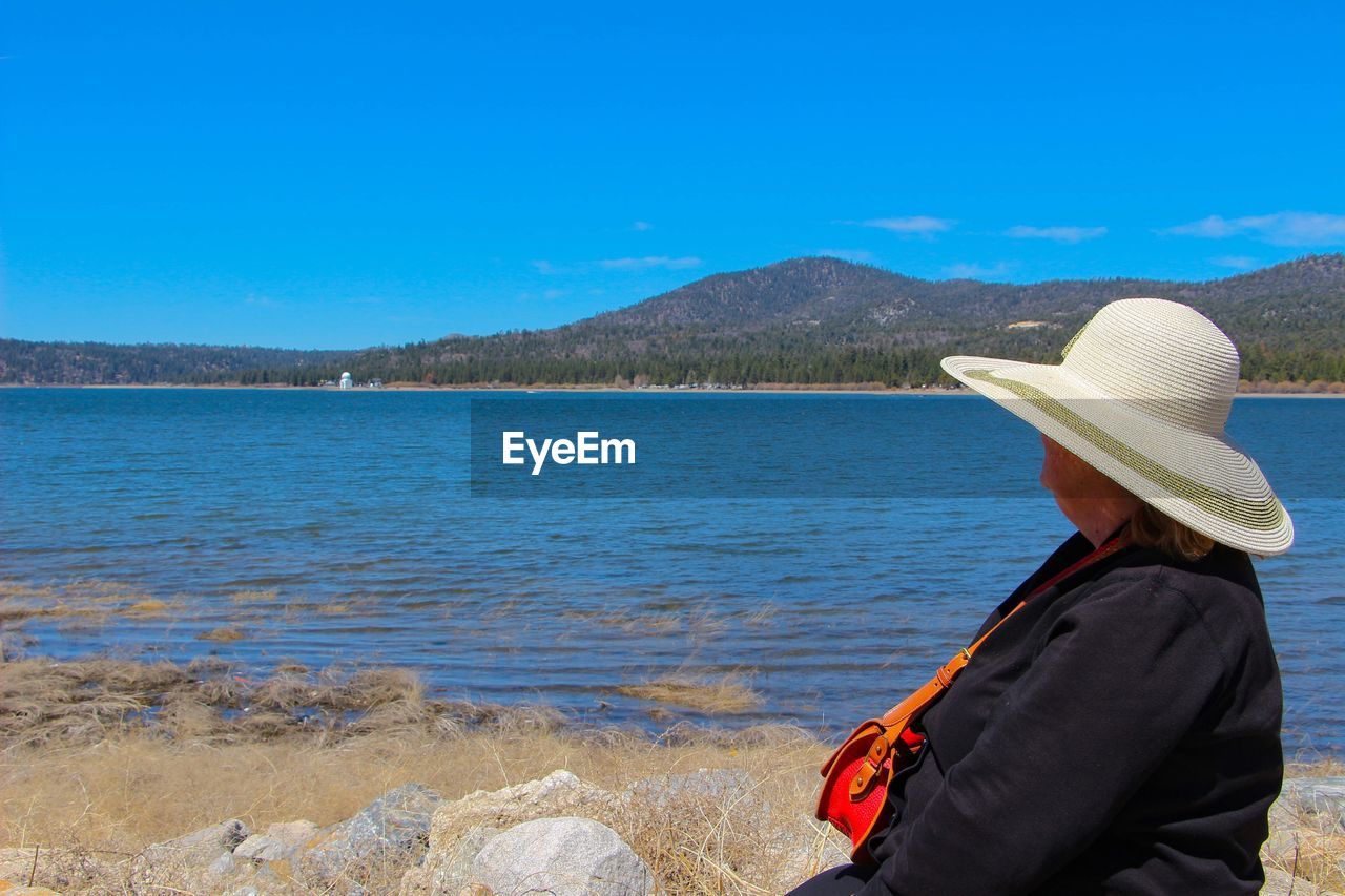 Side view of woman looking at lake against blue sky