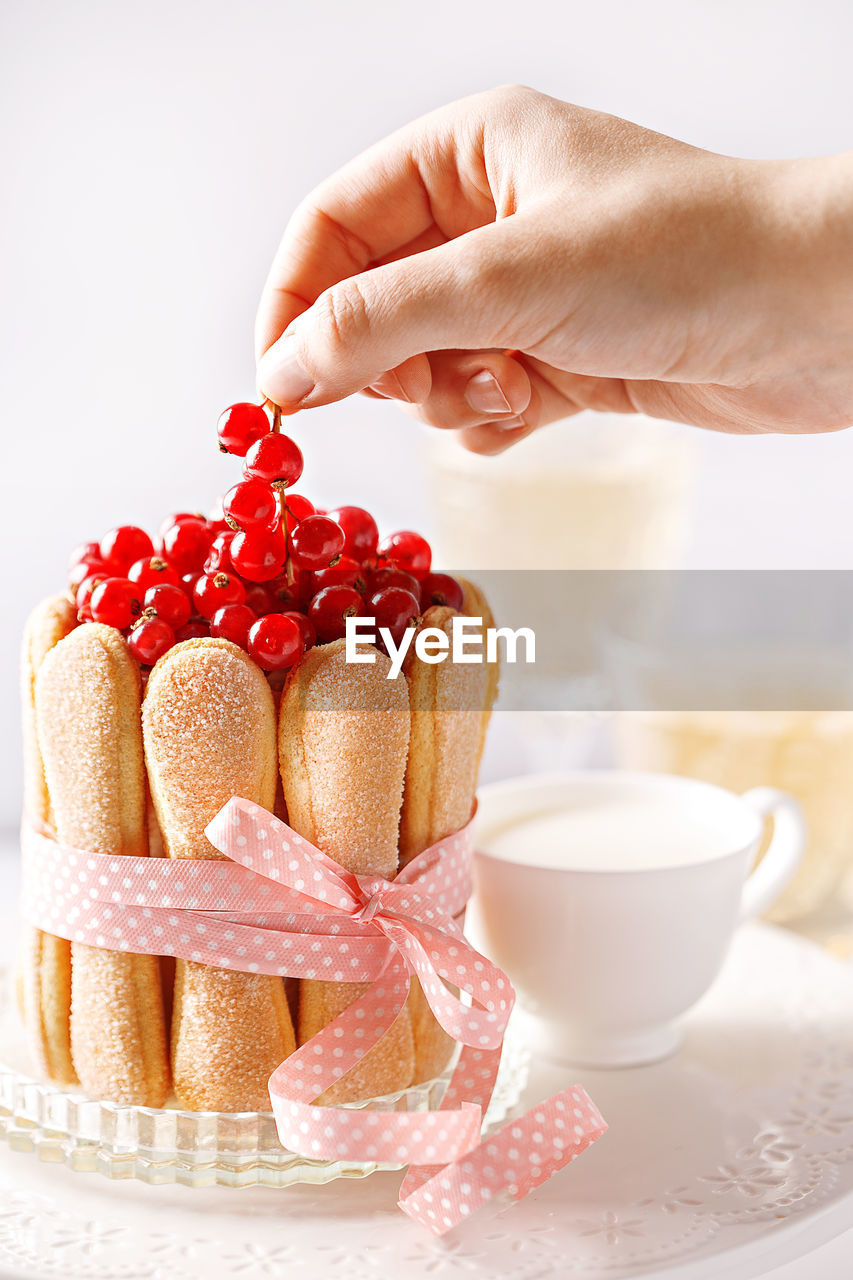 Cropped image of woman hand placing red currants on ladyfinger cake at table