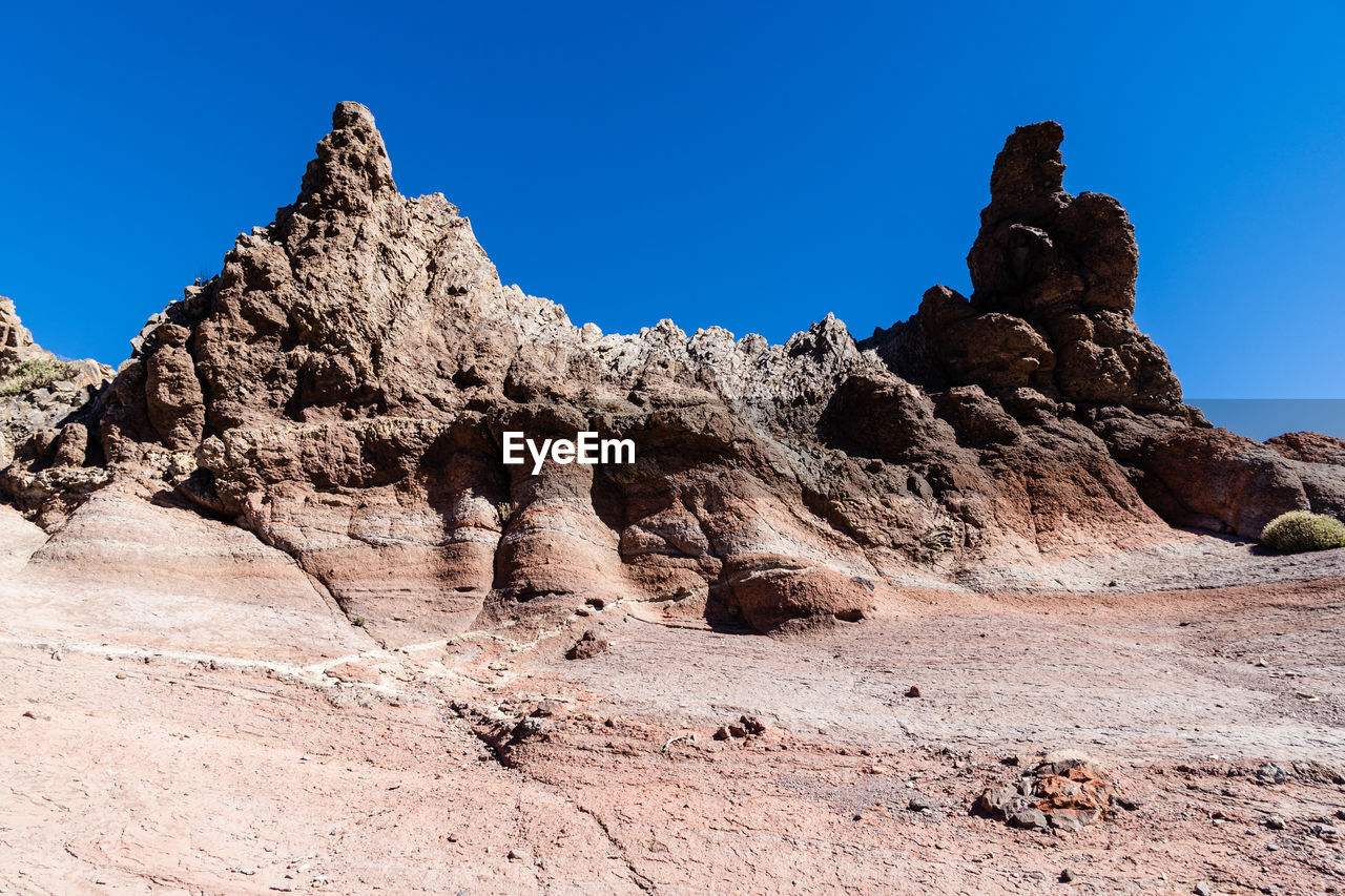 Low angle view of rock formations with a shade of pink against clear blue sky