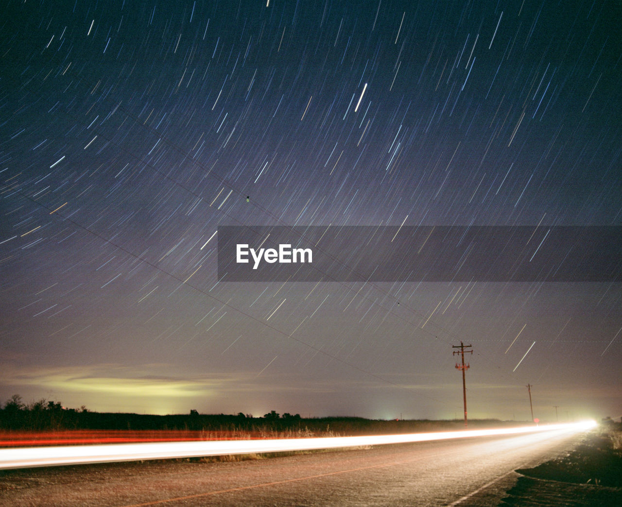 Star trails above road with long exposure car and telephone pole