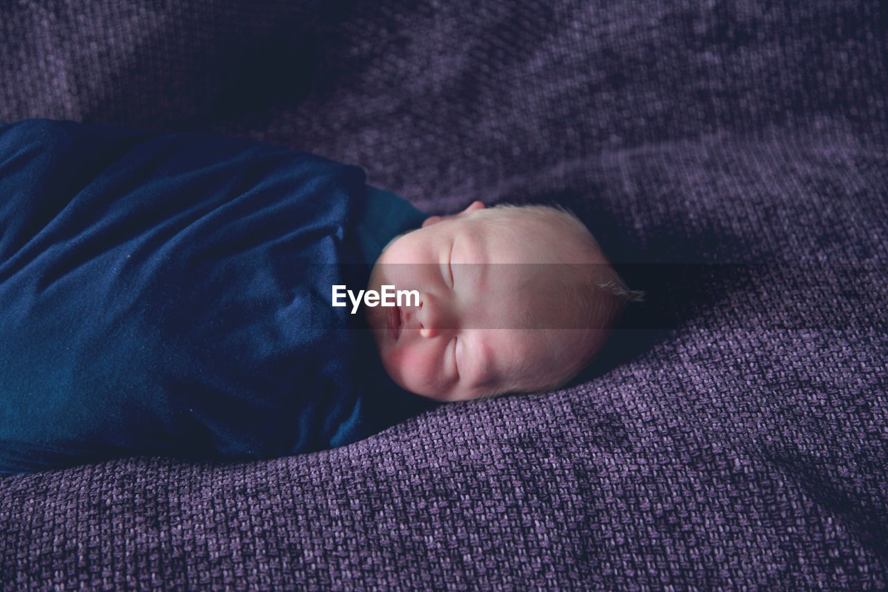 High angle view of newborn sleeping on purple fabric