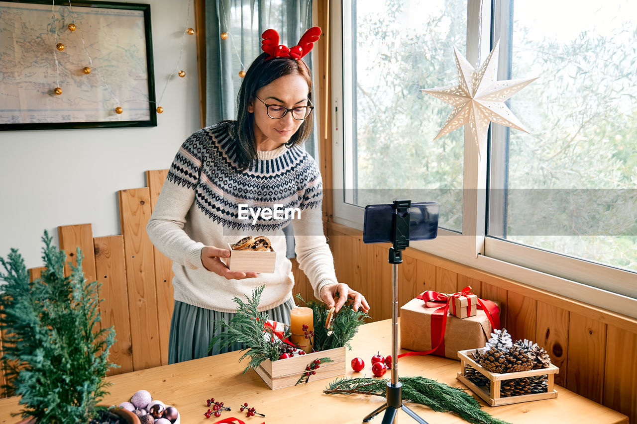 Female florist blogger making winter ikebana with pine branches, candle and christmas decorations