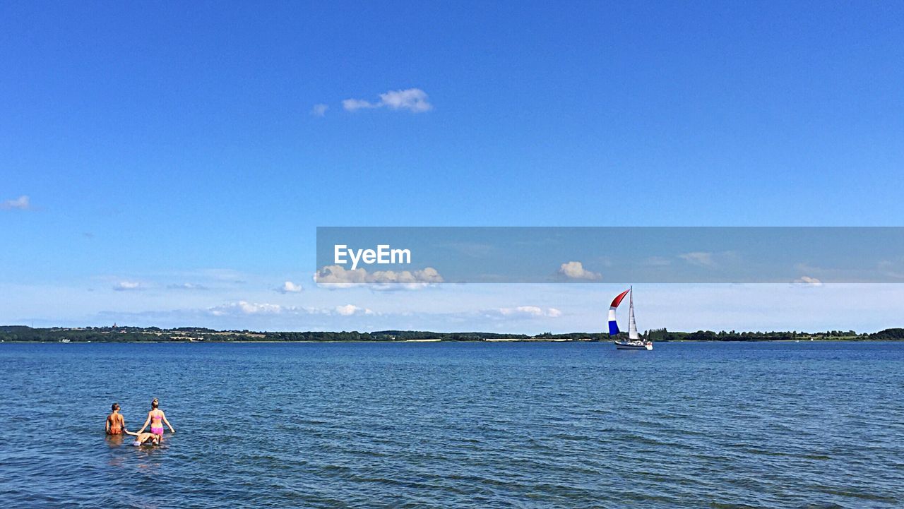 Children enjoying in sea against blue sky on sunny day