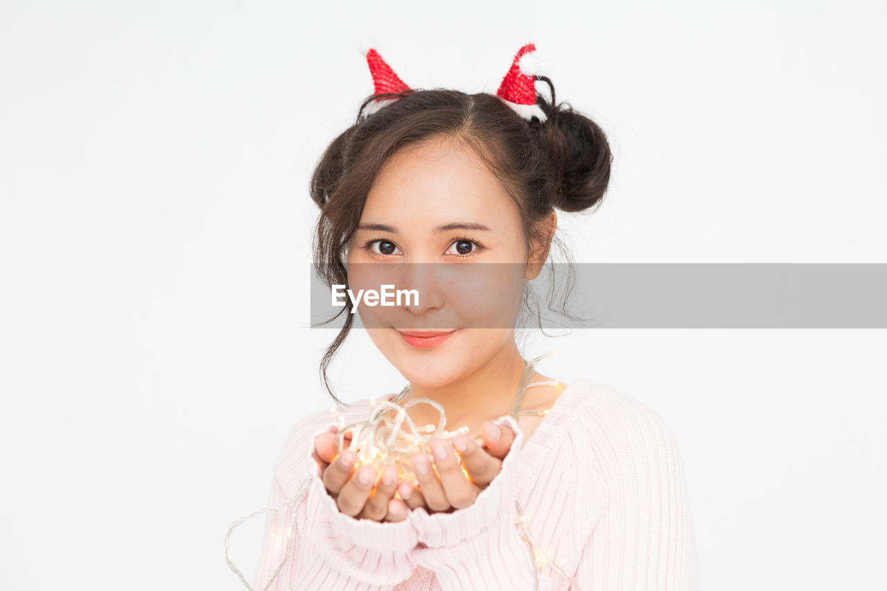 Beautiful asian woman wearing santa hat and wearing pink sweater holding christmas lights