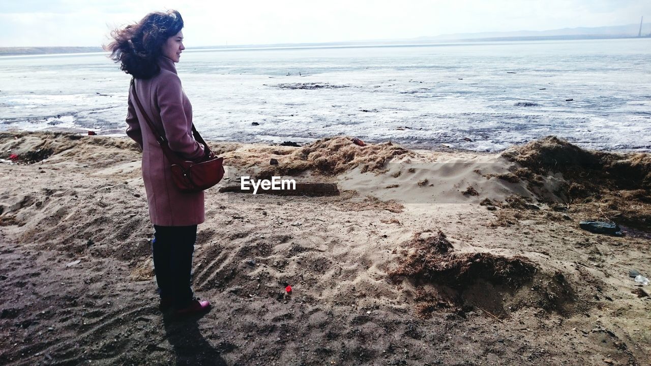 REAR VIEW OF WOMAN STANDING AT BEACH