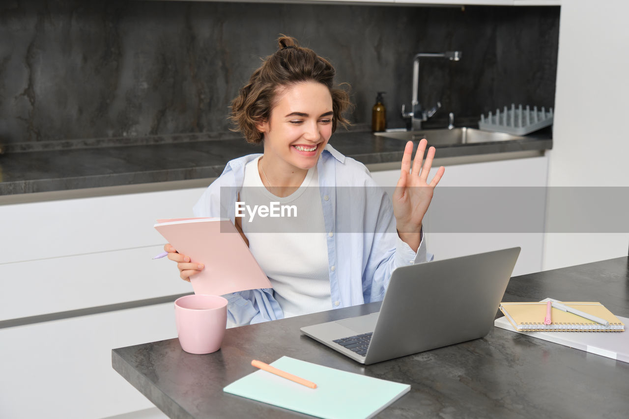 portrait of smiling young woman using laptop while sitting on table