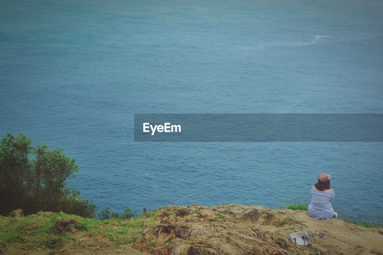 Rear view of woman looking at sea while sitting on land