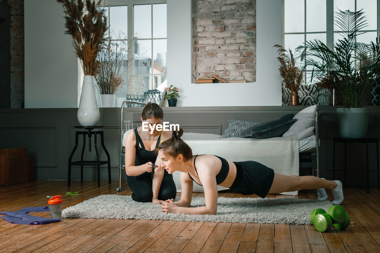 . home workout with a friend, the trainer monitors the plank time on the stopwatch