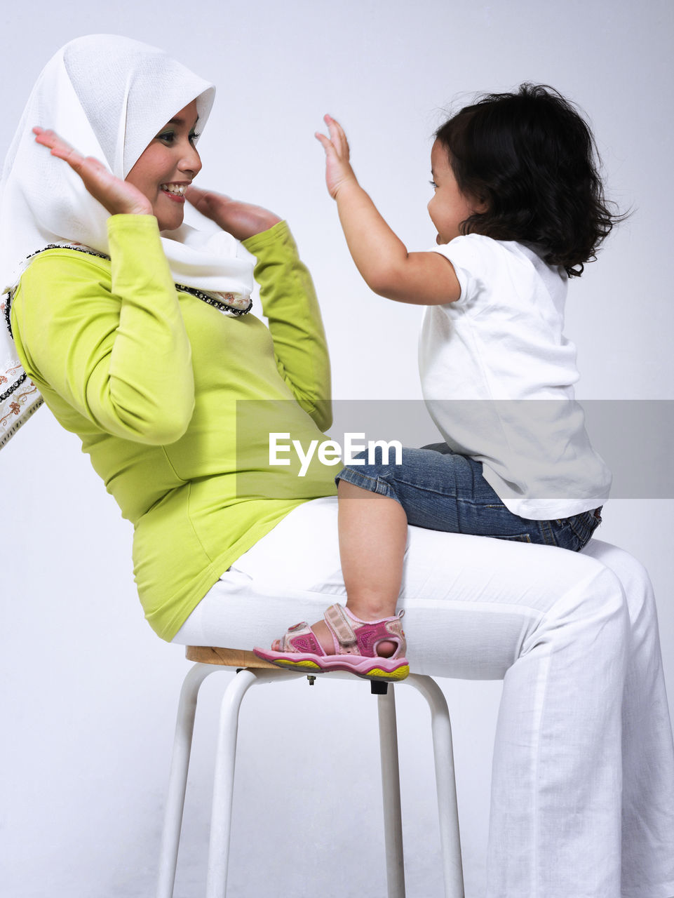 Side view of playful mother and daughter sitting on seat over white background
