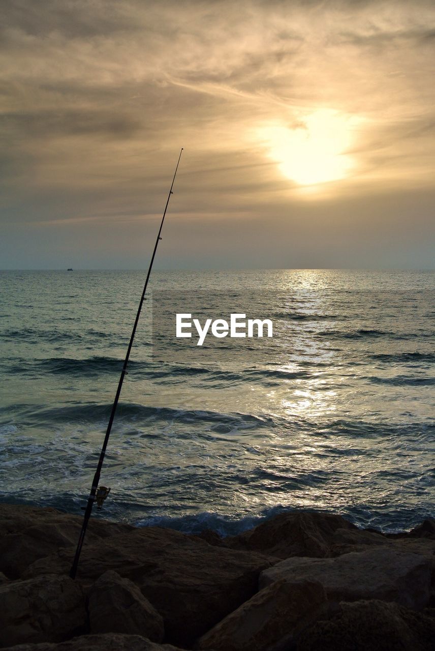 Fishing rod on rocks against sea during sunset