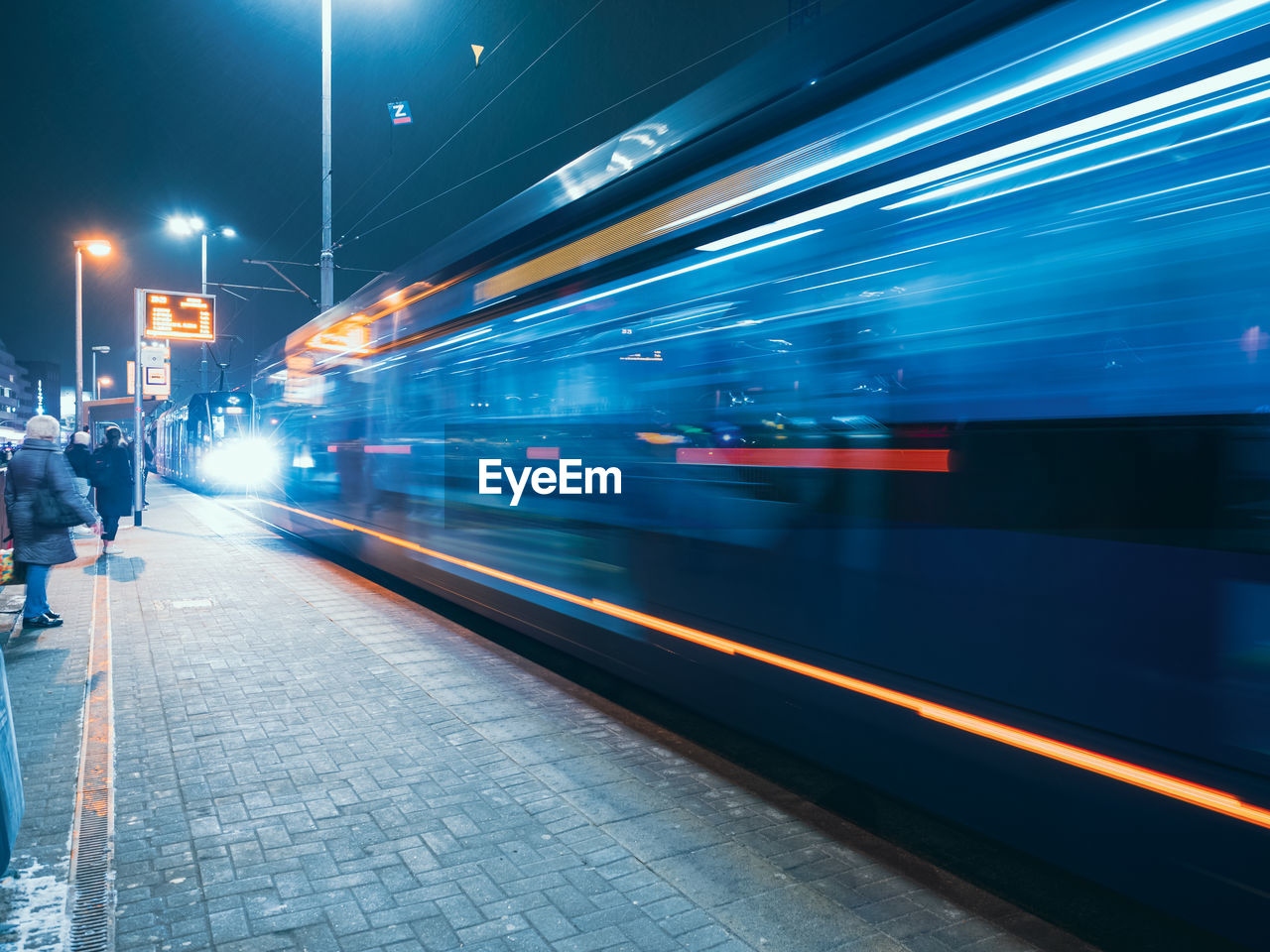 The tram leaves the stop in night city, motion blur view