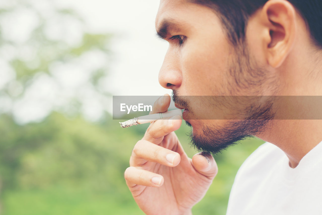 Man smoking cigarette against tree