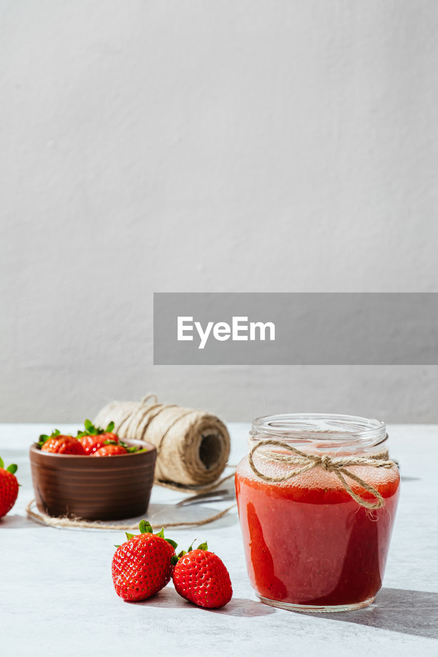 Composition with fresh homemade strawberry juice in glass jar wrapped with twine placed on marble surface with whole berries