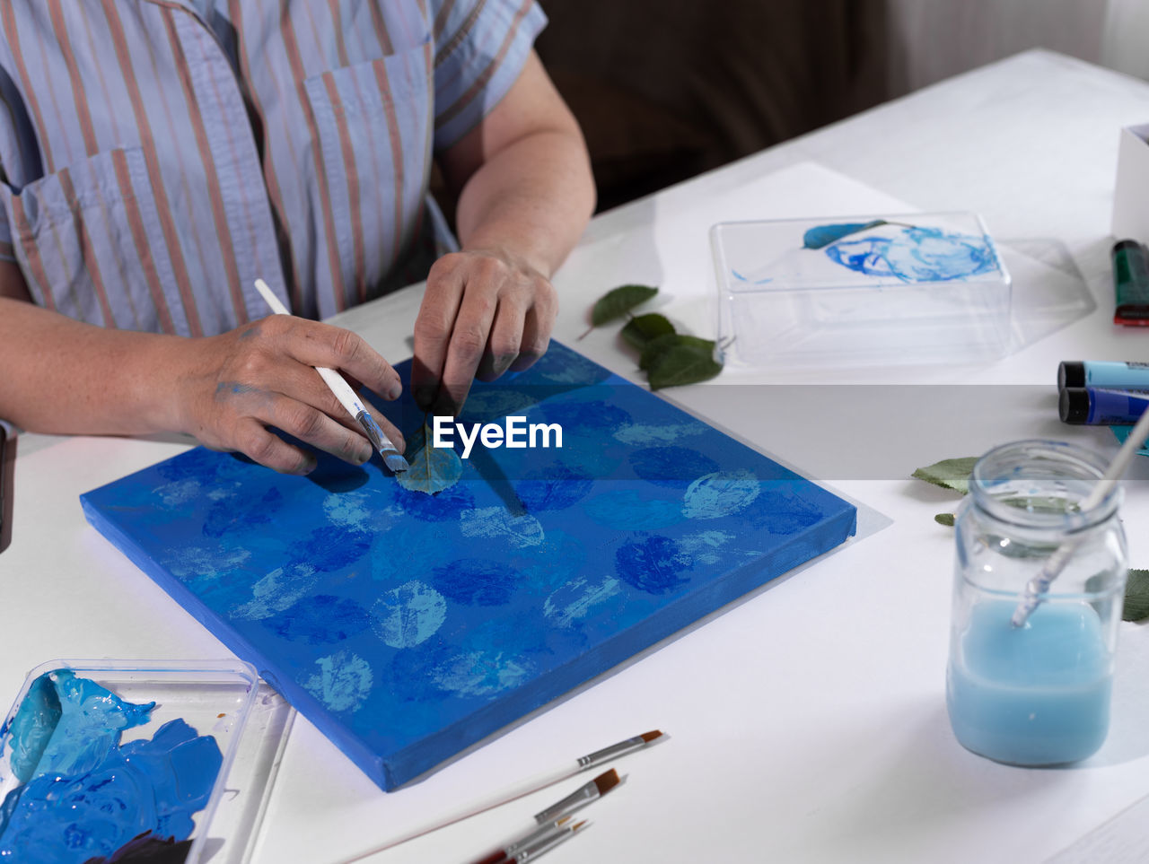 A woman paints a picture with a sheet of wood and acrylic paints