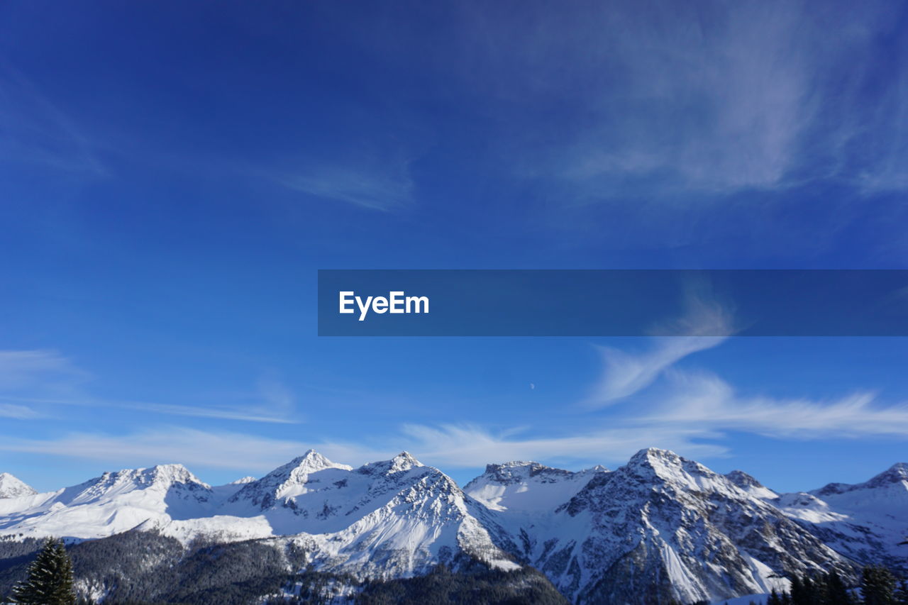 Scenic view of snowcapped mountains against blue sky