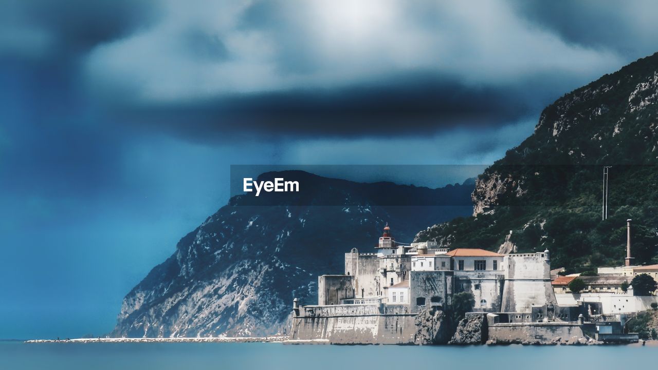 Buildings by sea against cloudy sky