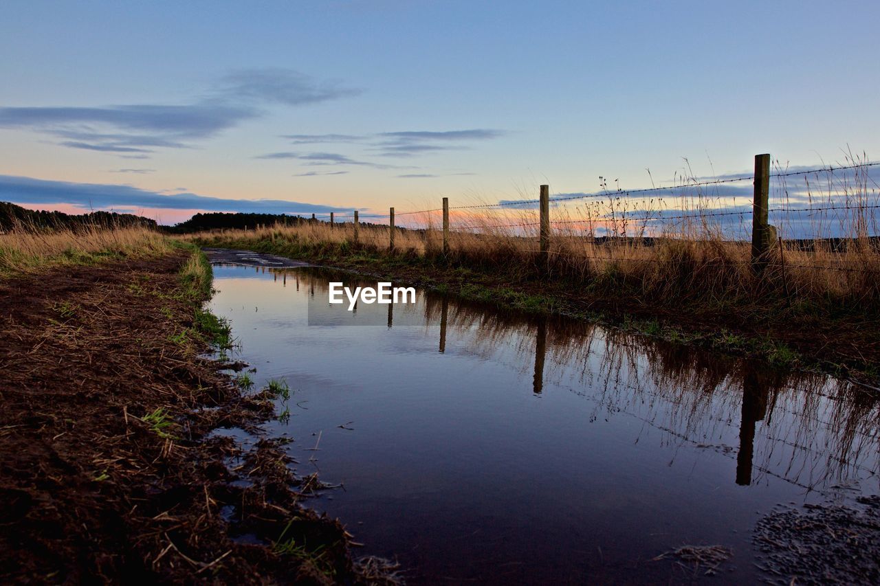 Stream on field against sky during sunset