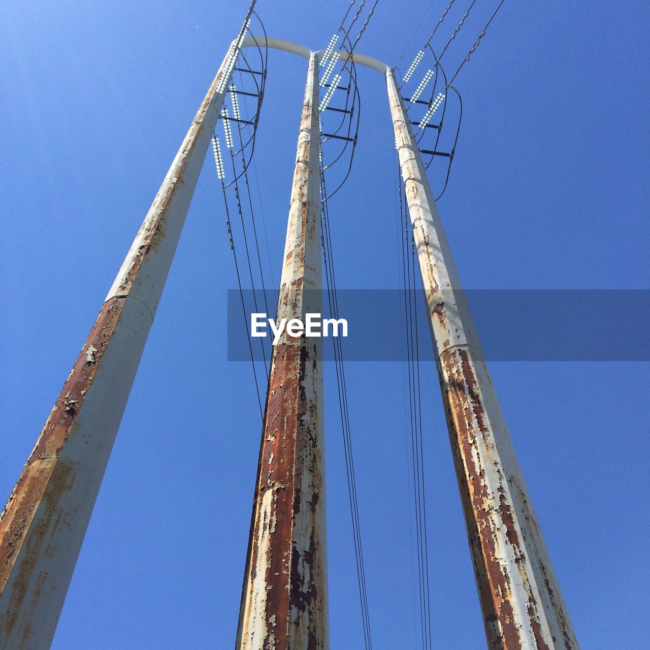 Low angle view of electricity pylons against clear blue sky
