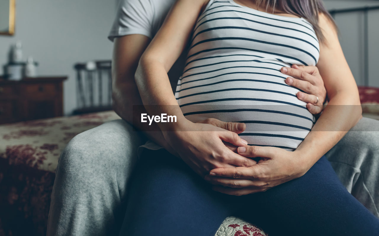 Midsection of couple sitting on bed at home