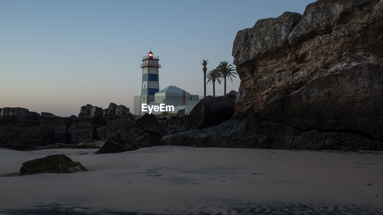 LIGHTHOUSE BY BUILDINGS AGAINST SKY