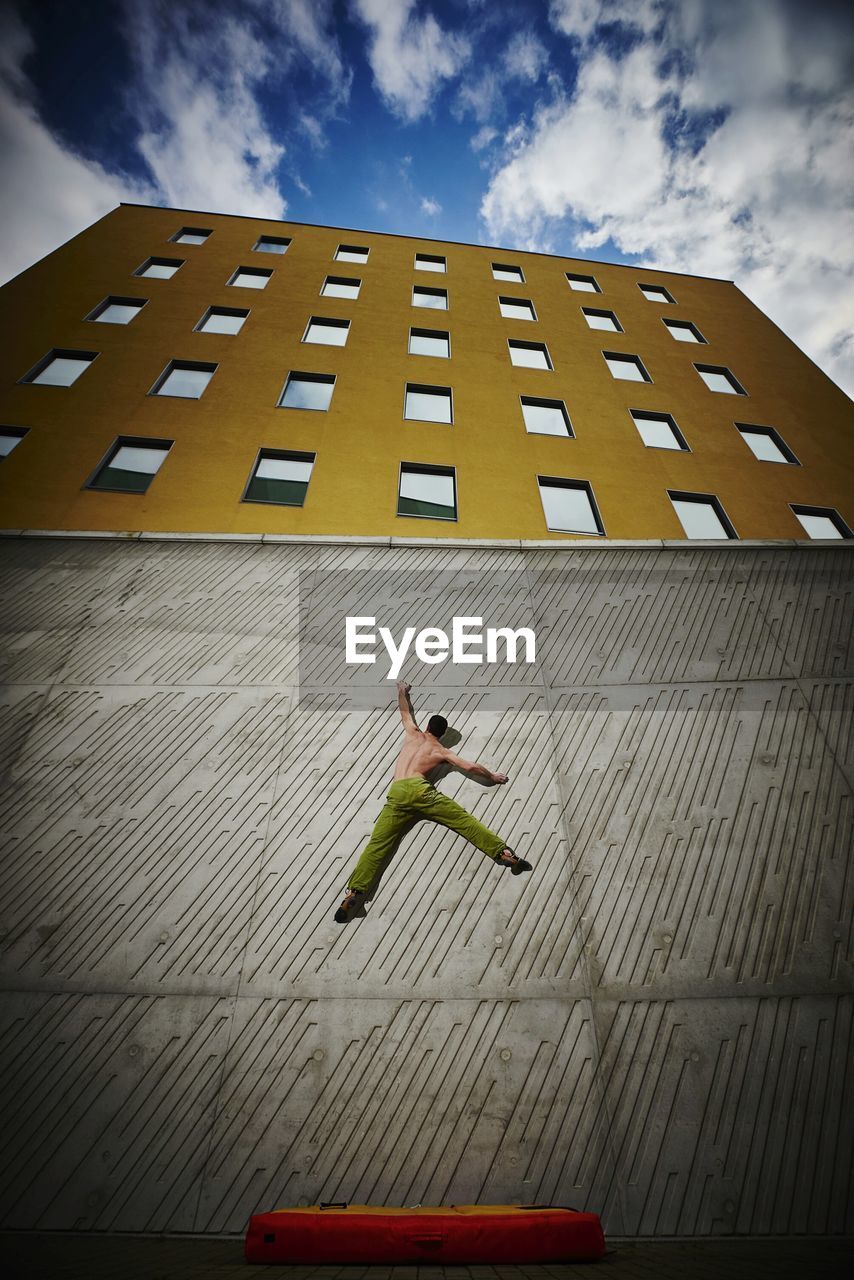 Low angle view of man climbing wall against sky
