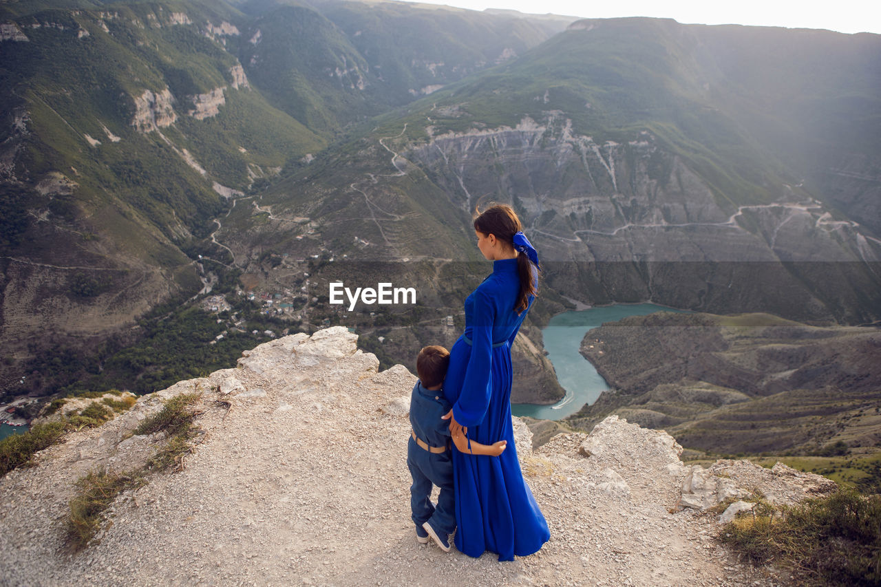 Mother in a blue dress with her son stands on the cliff of the sulak canyon in dagestan