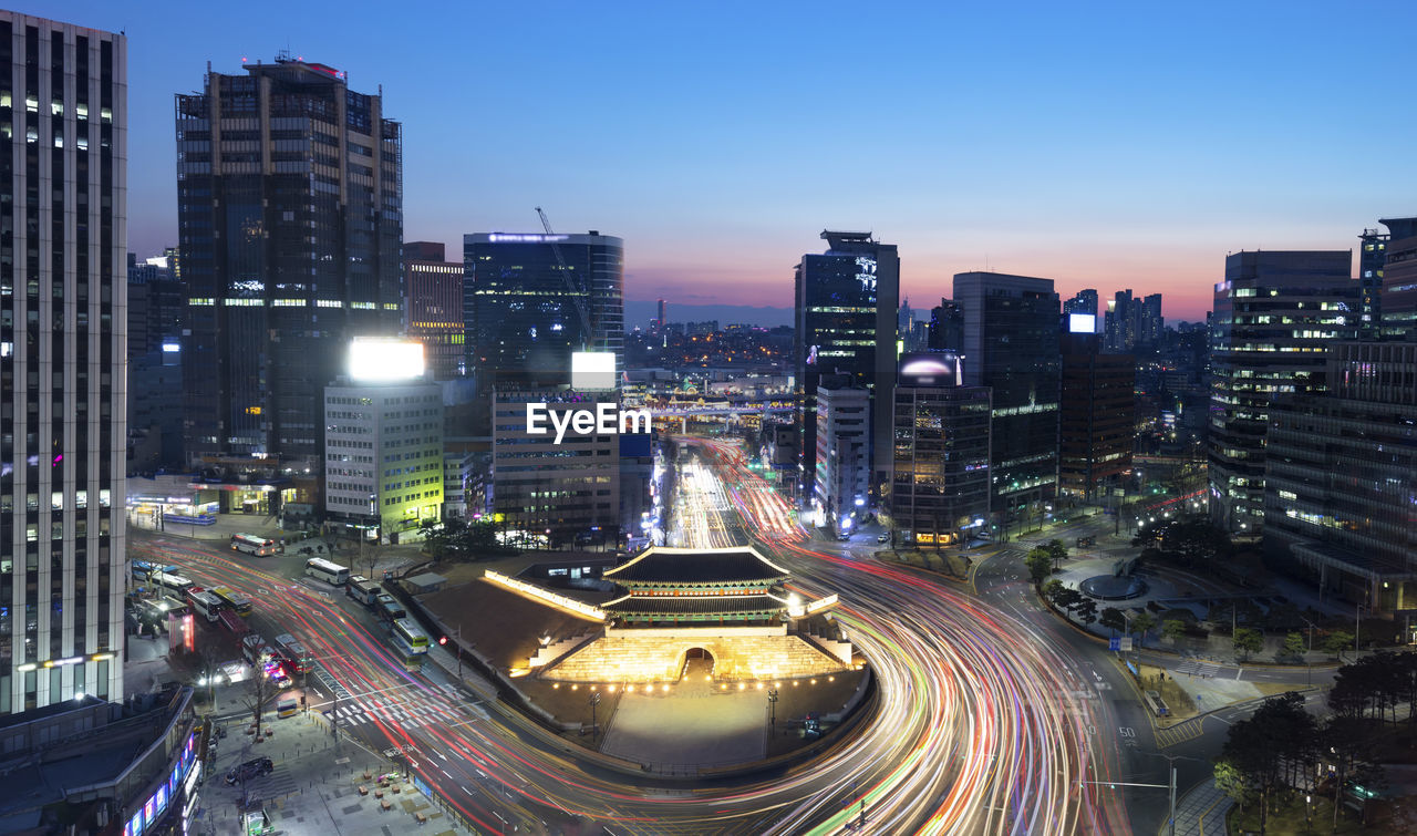 HIGH ANGLE VIEW OF ILLUMINATED STREET AMIDST BUILDINGS IN CITY