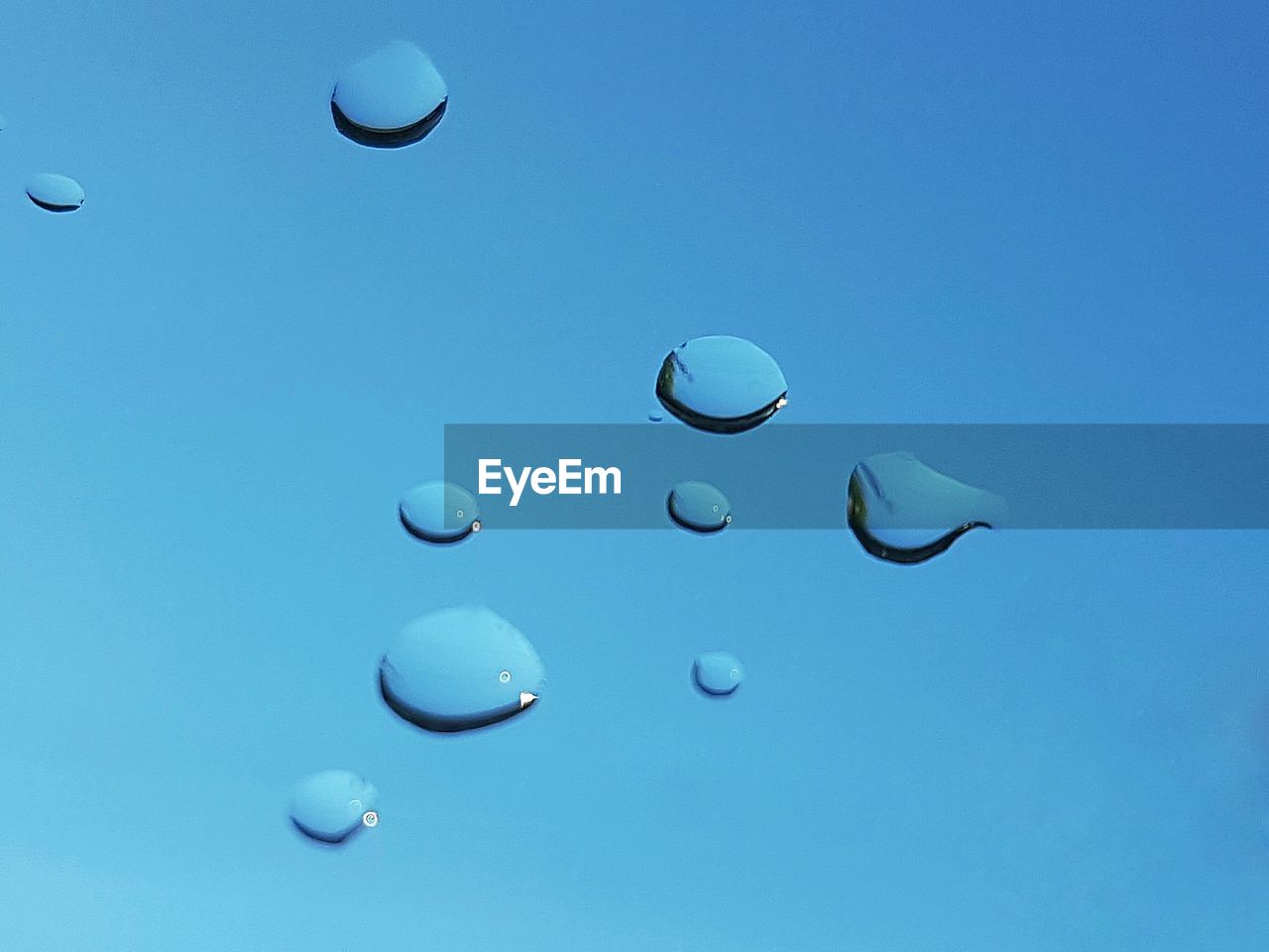 Close-up of water droplets on window against blue sky background