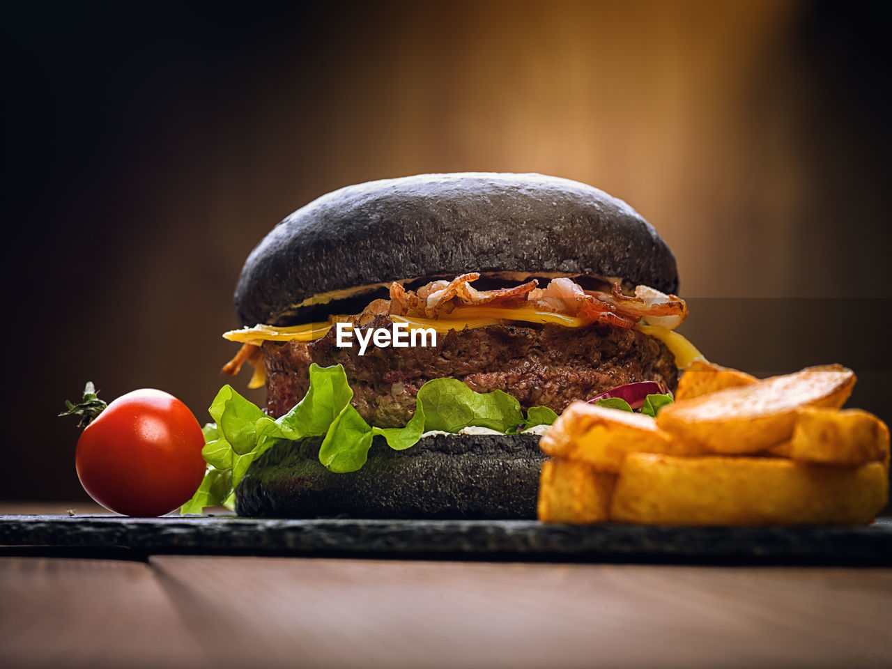 Black burger on a stone plate. cherry tomatoes. fried potatoes.
