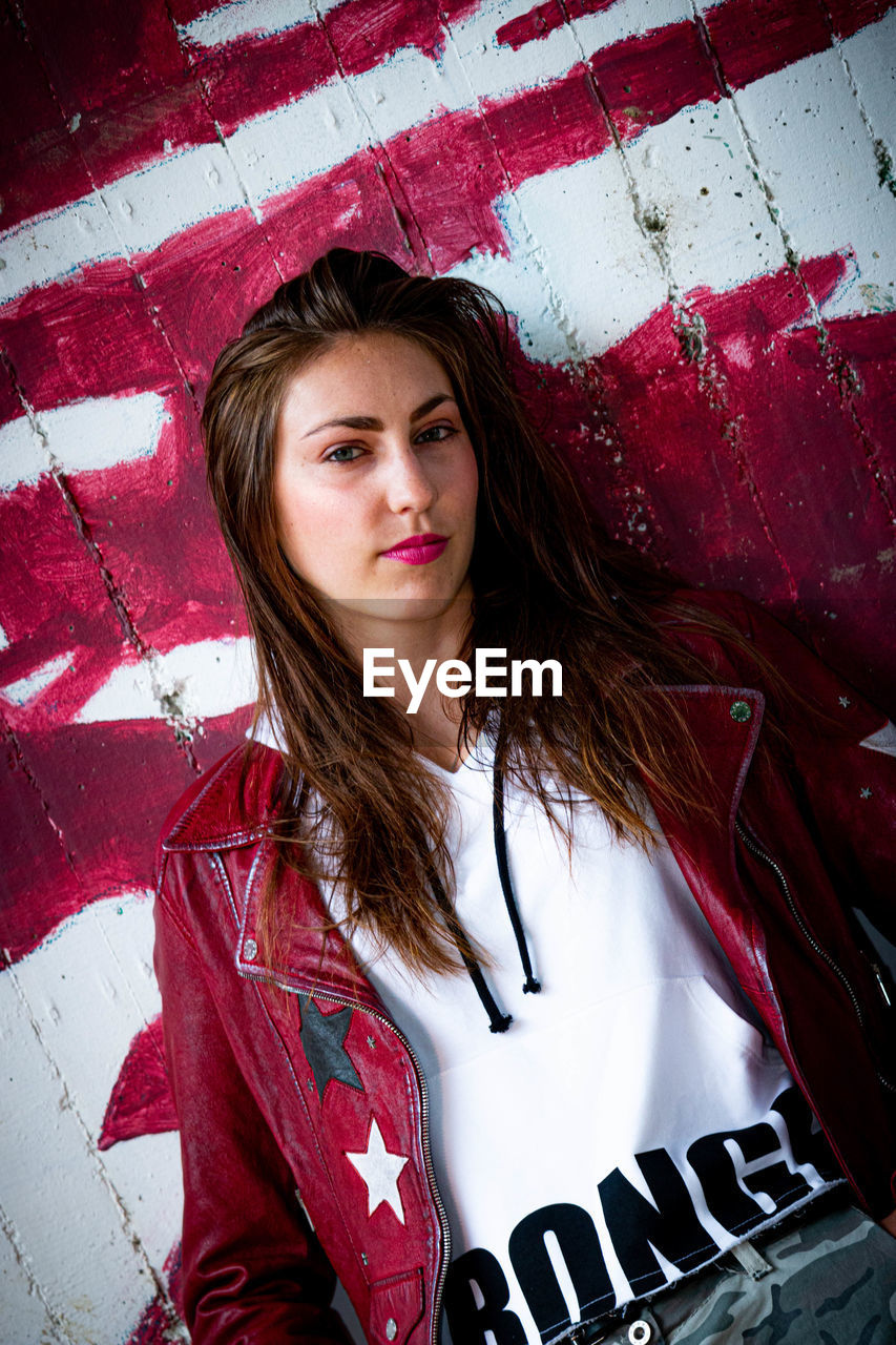 PORTRAIT OF A BEAUTIFUL YOUNG WOMAN STANDING AGAINST WALL