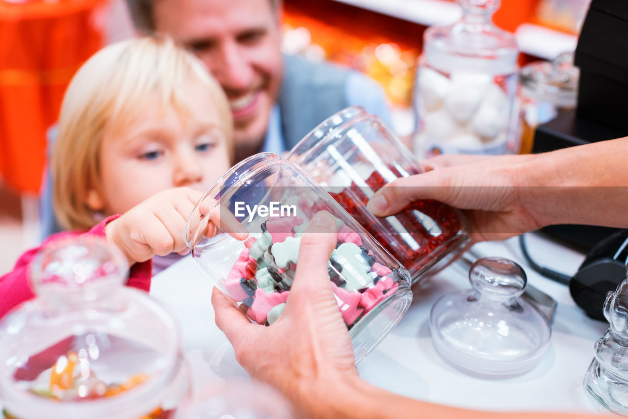 Sales clerk holding jars with candies by girl at store