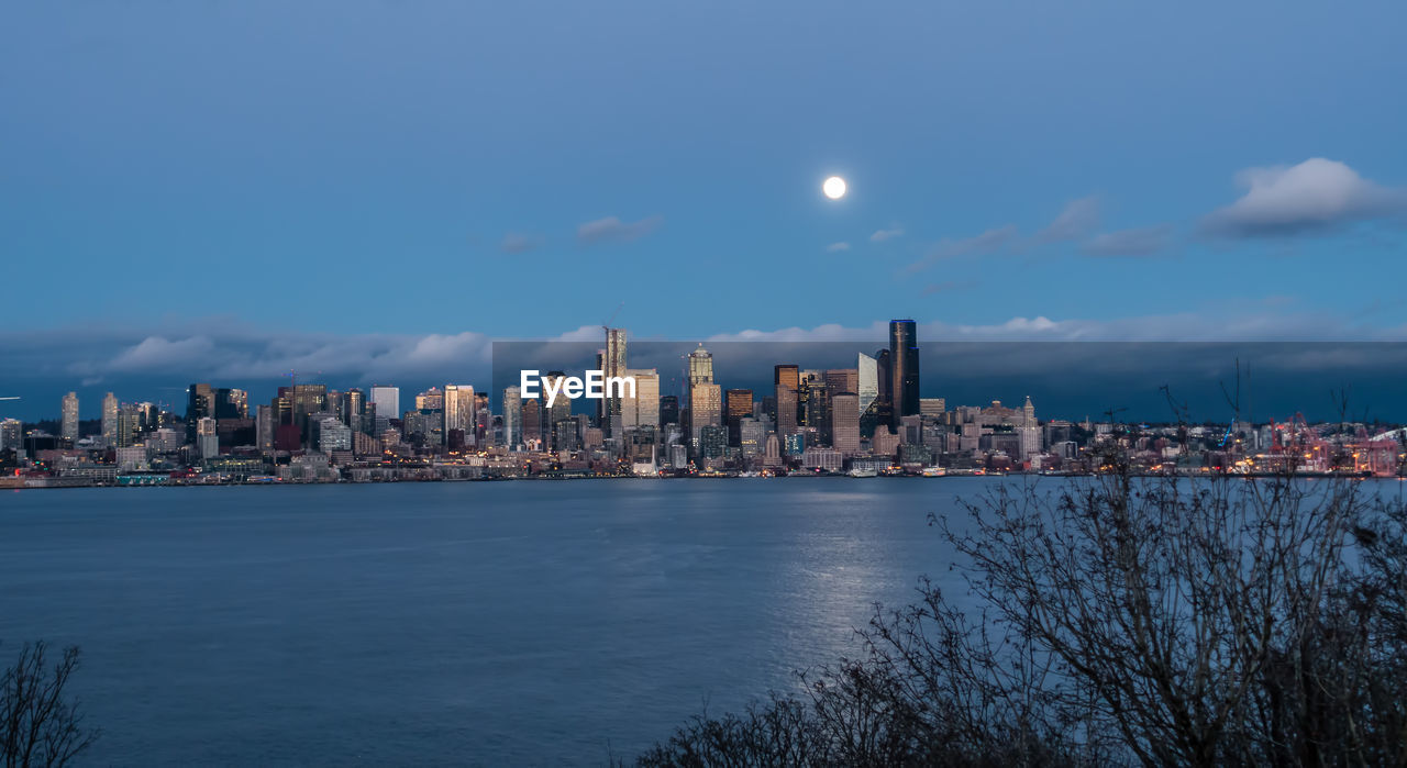 A full moon shines above the seattle skyline.