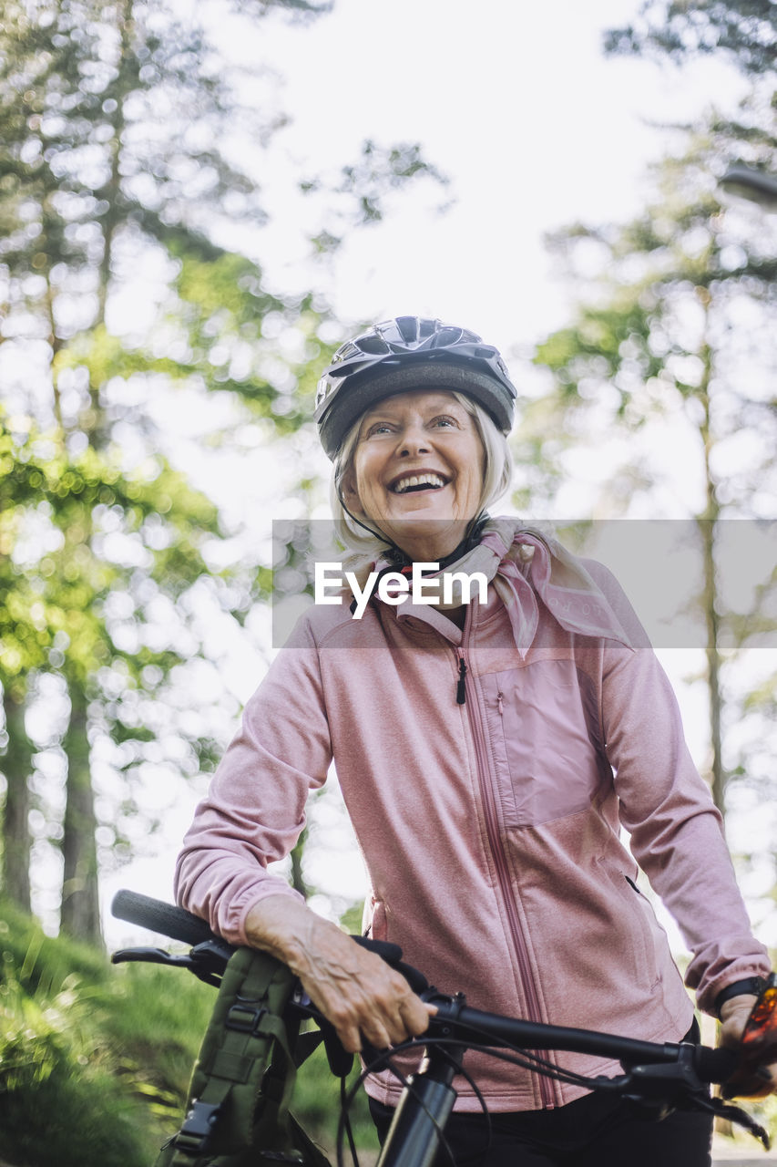 Smiling senior woman looking away while standing with cycle