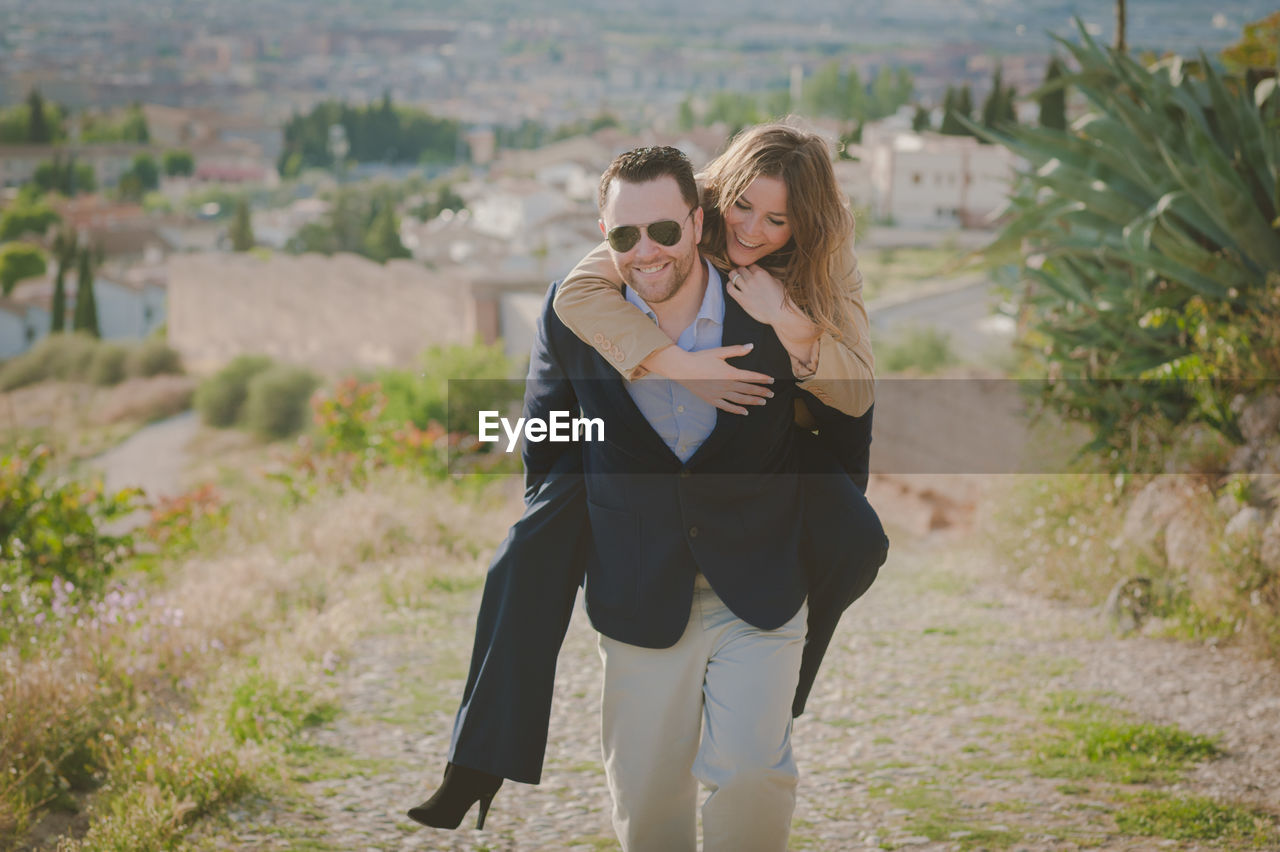 Man giving piggy back ride to happy woman standing on land