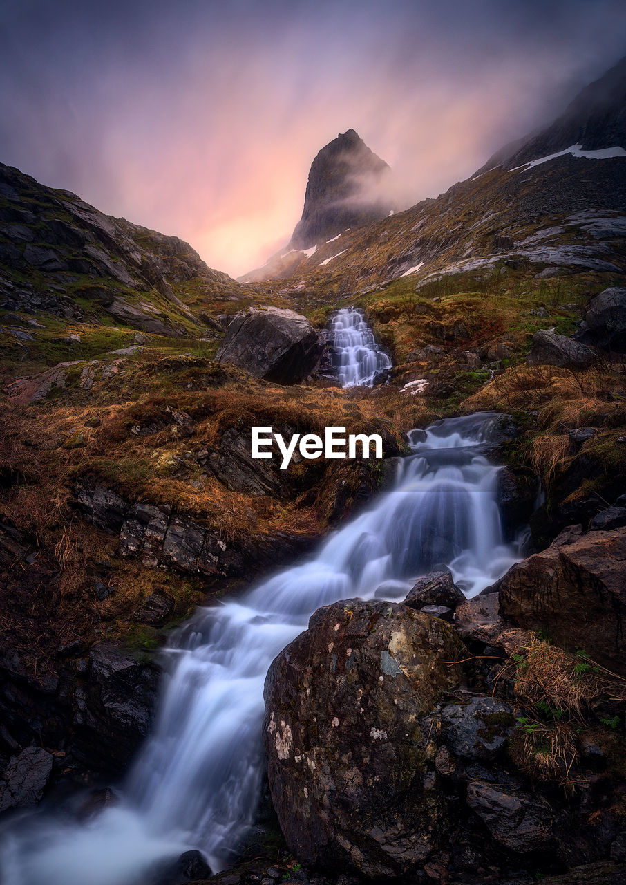 Scenic view of waterfall against cloudy sky at sunset