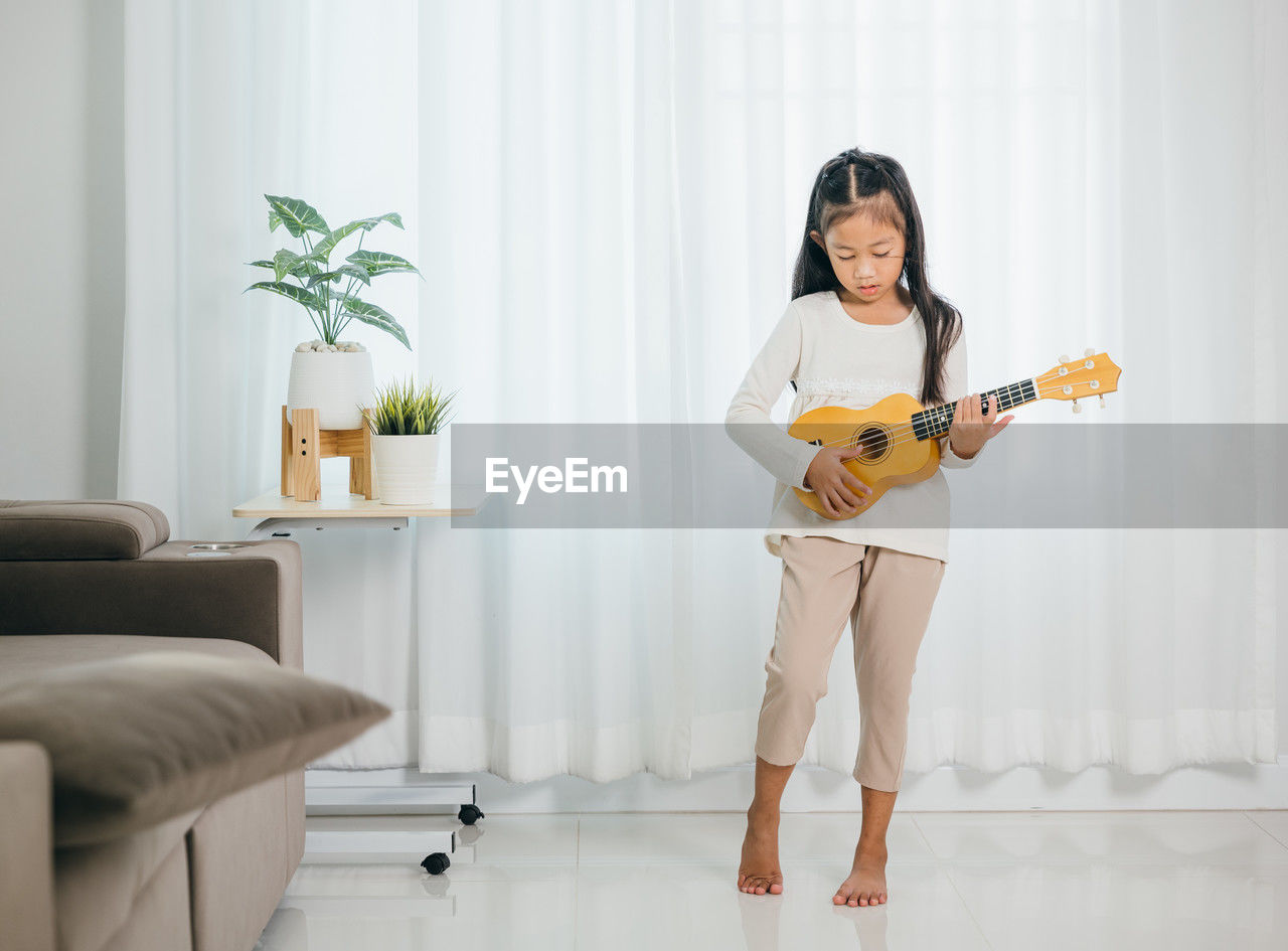 portrait of young woman playing guitar while sitting on sofa at home