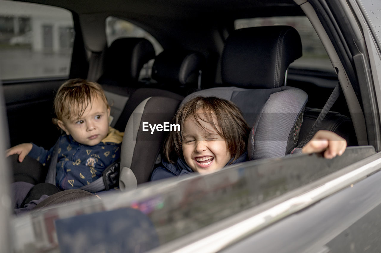 Happy siblings sitting on backseat of car