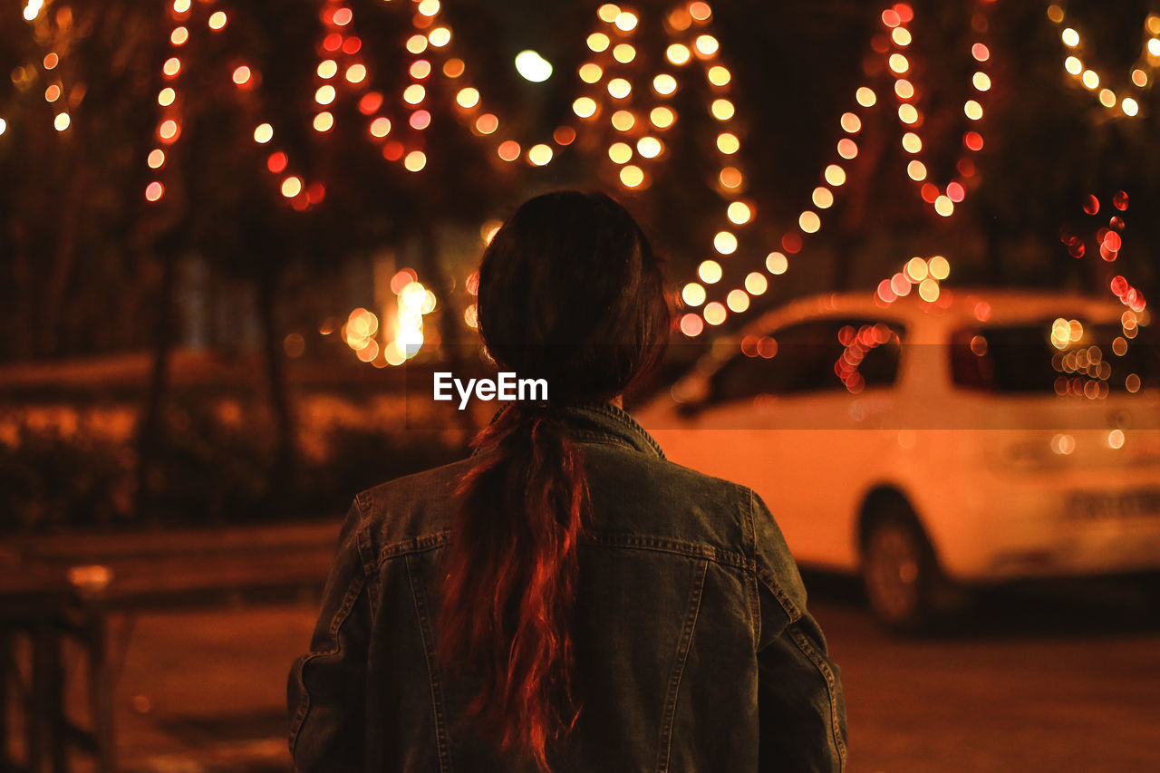 Rear view of woman standing on illuminated street at night