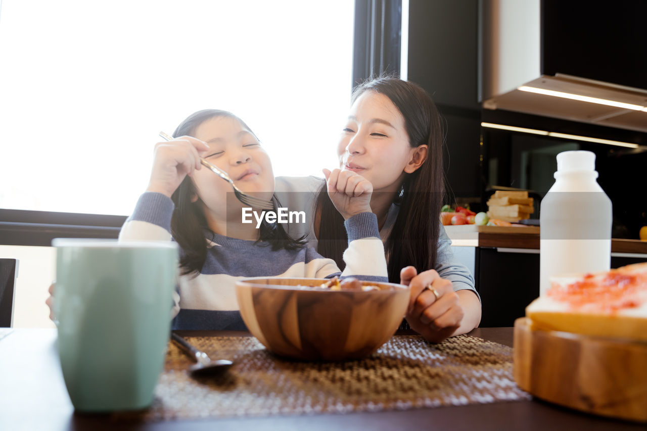 Girl sitting with mother in kitchen at home