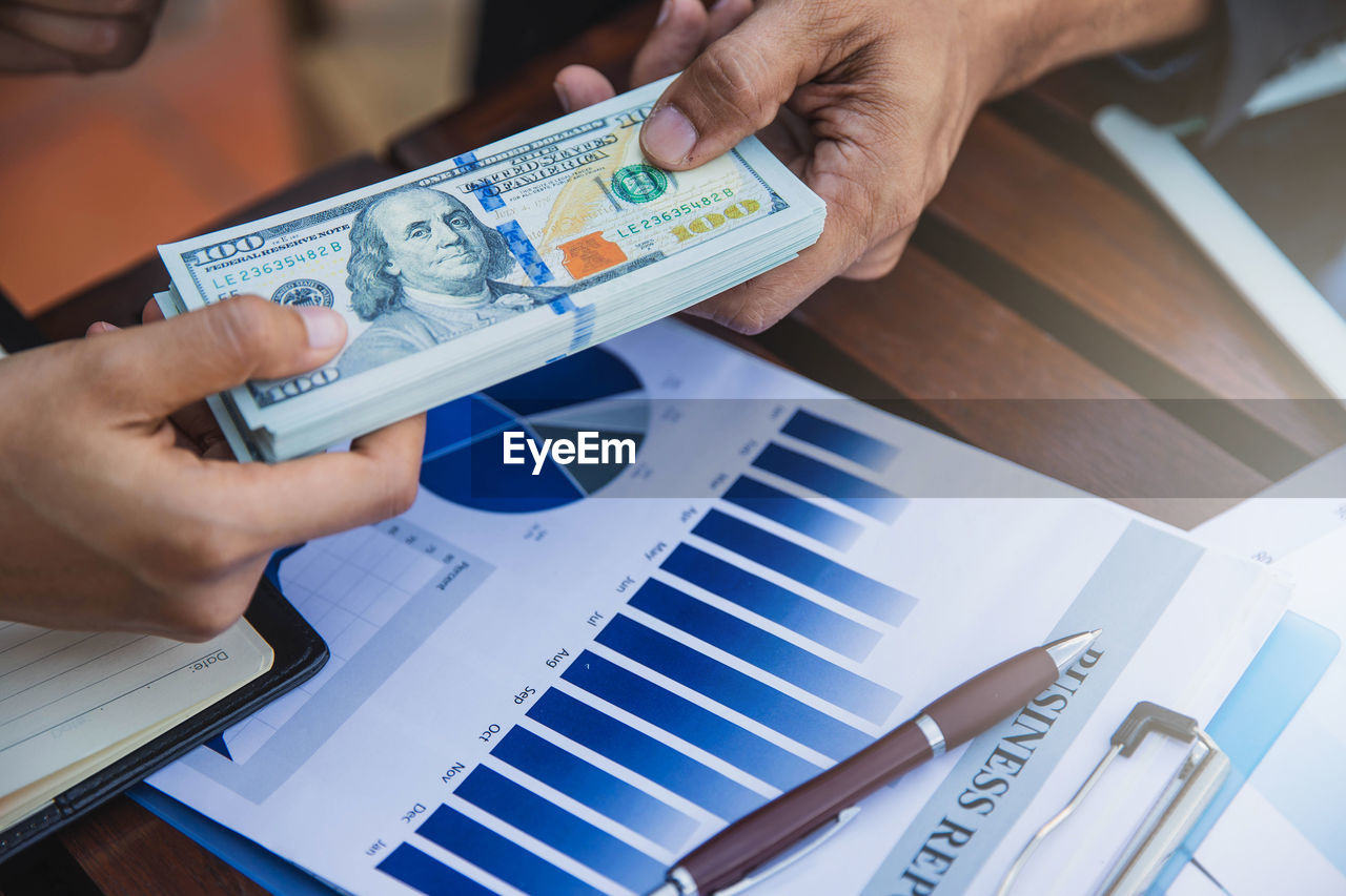 Cropped hands of business colleagues holding paper currency on table