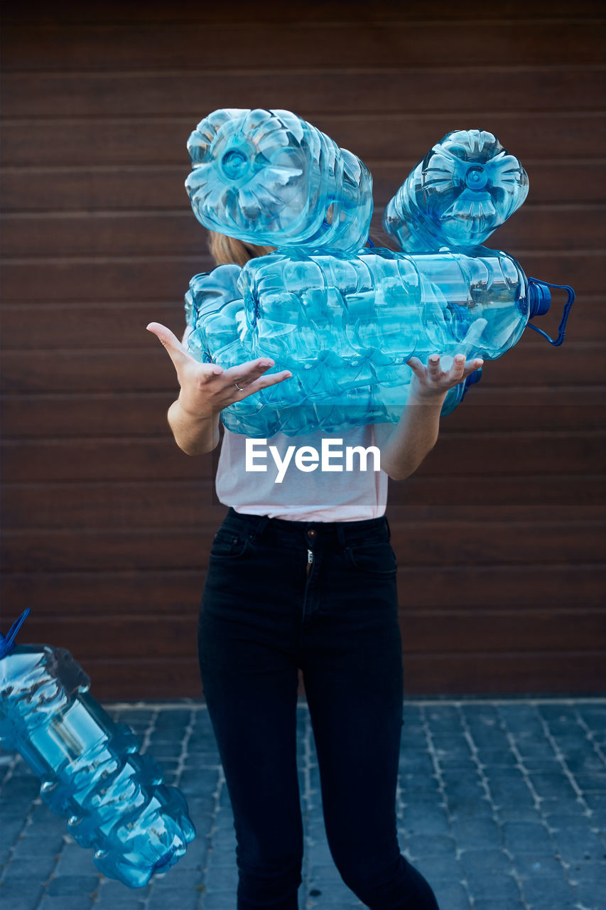 Young woman throwing out empty used plastic water bottles into trash bin. collecting plastic waste