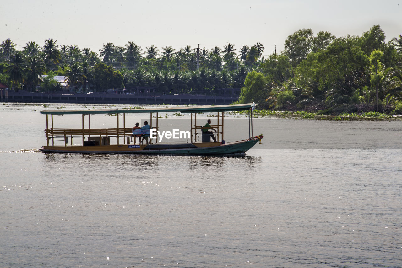 PEOPLE ON BOAT IN RIVER AGAINST TREES